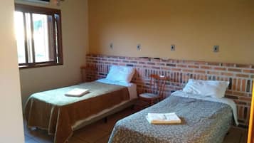 Una habitación con dos camas individuales, cabecera de ladrillo, ventana y ventilador de techo.
