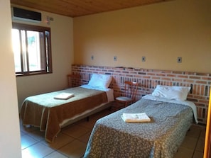 A room with two single beds, a brick headboard, a window, and a ceiling fan. - Pousada do Pampa  (Jaguarão)