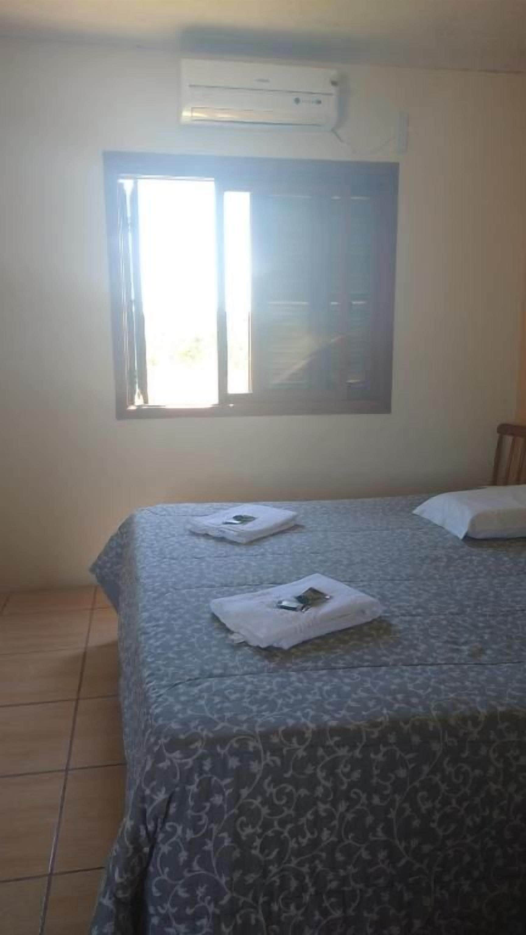 Ein Zimmer mit einem Bett, einem Fenster mit Jalousien und einer Klimaanlage.