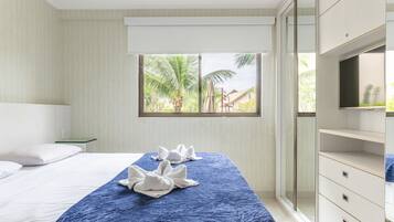 A hotel room with a bed, a window with a view of palm trees, and a wardrobe.