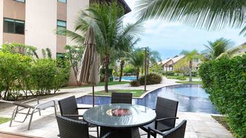 A poolside area with a round table and chairs, surrounded by palm trees and a swimming pool.