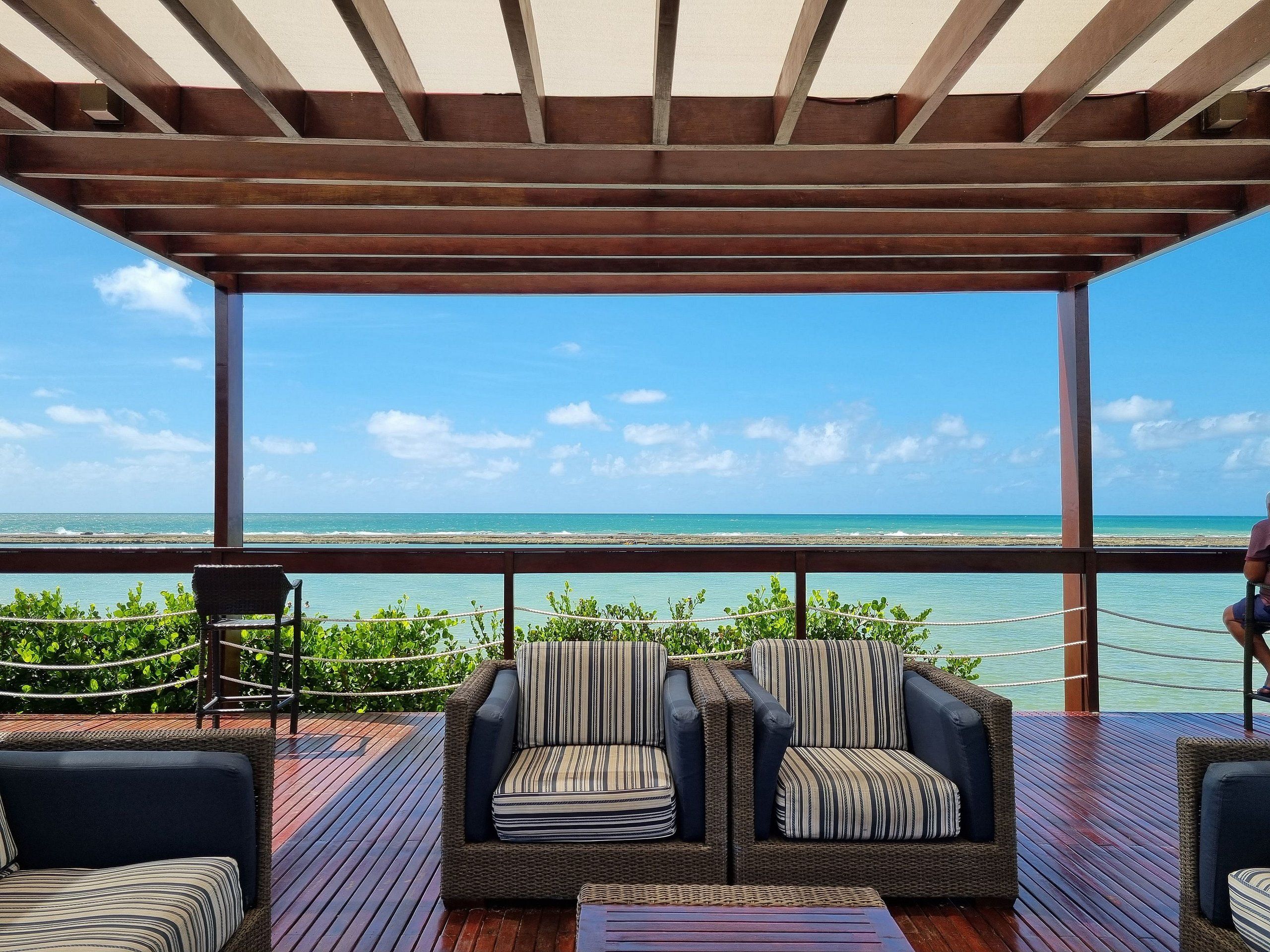 Un espace extérieur aménagé, abrité et doté de mobilier en osier, avec vue sur une plage.
