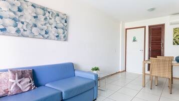 A room with a blue sofa, a small table with a plant, and a door with a welcome sign.