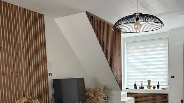 A modern living room with a TV, wooden panel wall, staircase, and a hanging light fixture. - Vrbo Property (Croix)