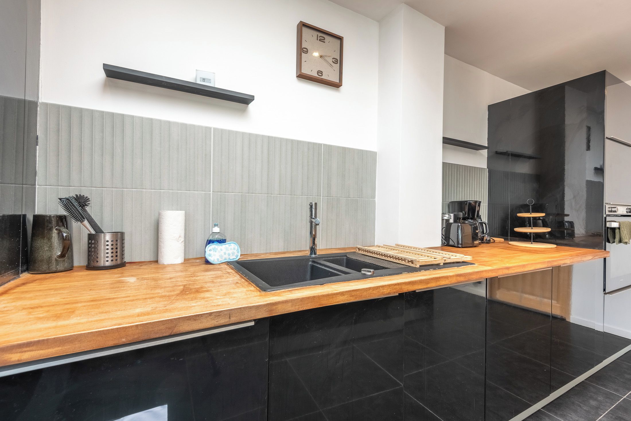 A modern kitchen with a wooden countertop, black cabinets, a built-in sink, and a coffee maker.