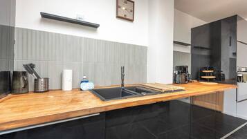 A modern kitchen with a wooden countertop, black cabinets, a built-in sink, and a coffee maker.