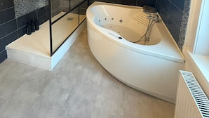 A modern bathroom with a freestanding bathtub, a glass shower enclosure, and dark tiled walls. - Vrbo Property (Croix)