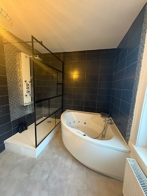 Un baño moderno con una bañera independiente, cabina de ducha con mampara de vidrio y paredes revestidas con baldosas oscuras.