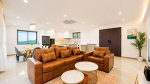 Ein modernes Wohnzimmer mit einem braunen Leder-Modulsofa, zwei runden Couchtischen und einem Essbereich mit Tisch und Stühlen.