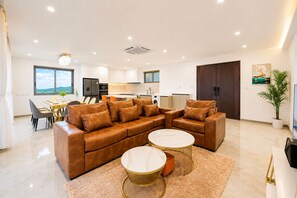 Un salon moderne avec un canapé d’angle en cuir marron, deux petites tables rondes et un coin repas comprenant une table et des chaises.
