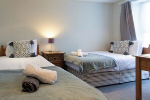 A hotel room with two beds, a bedside table, a lamp, and a window with curtains. - Charming 3-bedroom cottage in Porthleven with spectacular harbour views
3HARB (Porthleven)