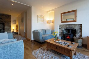 A cozy living room with a fireplace, a sofa, a coffee table with magazines, and a stone wall. - Charming 3-bedroom cottage in Porthleven with spectacular harbour views
3HARB (Porthleven)