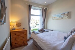A bedroom with a bed, a dresser, a window with curtains, and a painting on the wall. - Charming 3-bedroom cottage in Porthleven with spectacular harbour views
3HARB (Porthleven)