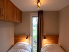 Ein Schlafzimmer mit zwei Betten, Holz-Kopfteilen und einem Fenster mit Vorhängen.