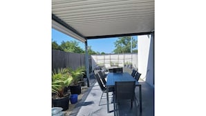 An outdoor patio with a table and chairs, surrounded by potted plants and a covered area. - Vrbo Property (Le Boulou)
