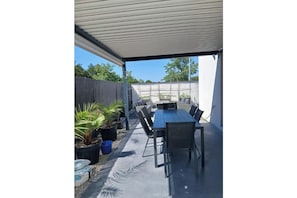 Eine Terrasse im Freien mit Tisch und Stühlen, umgeben von Kübelpflanzen und einem überdachten Bereich.