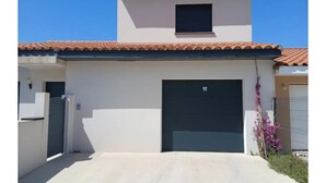 A modern building with a garage door, a small window, and a clear sky. - Vrbo Property (Le Boulou)