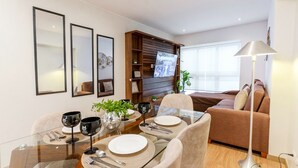 Uma área de refeições moderna com mesa de vidro, cadeiras e um sofá ao fundo.
