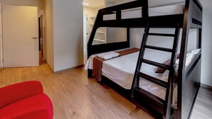 Quarto com beliche, piso de madeira, uma cadeira vermelha e porta branca.