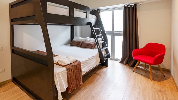Uma cama beliche com escada, uma cadeira vermelha e uma janela com cortinas.