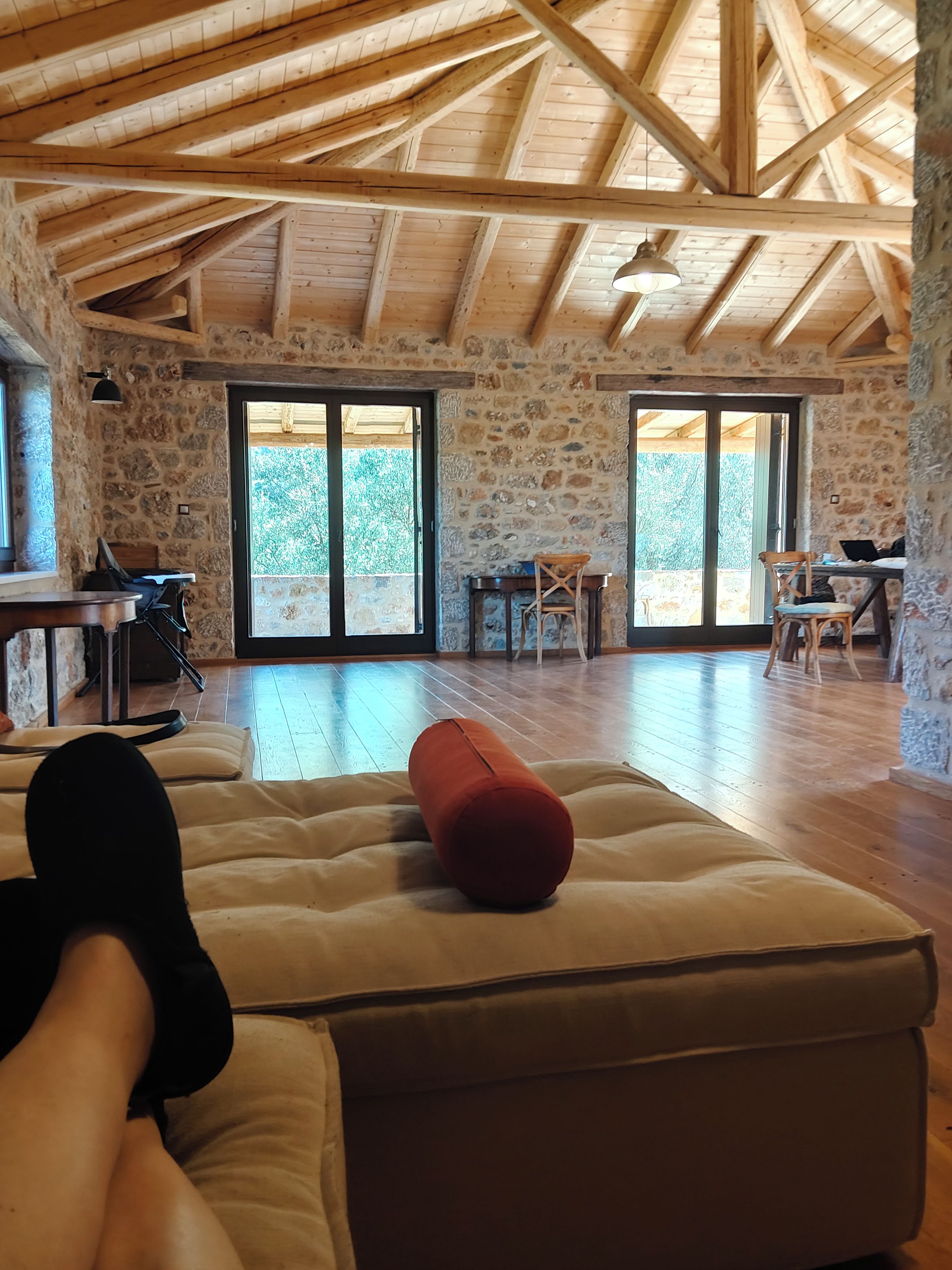 A spacious room with a high wooden ceiling, stone walls, and a large sliding glass door leading to an outdoor area.