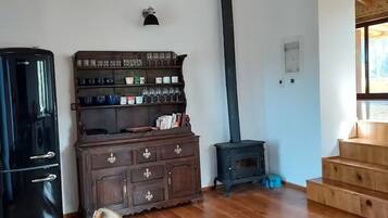 A room with wooden beams, a black stove, a wooden cabinet, and a dining table.