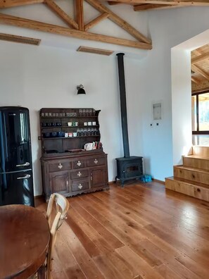 A room with wooden beams, a black stove, a wooden cabinet, and a dining table.