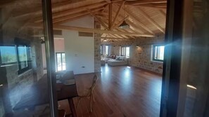 A spacious living area with a high ceiling and stone walls. There is a seating area with a sofa and a dining table with chairs.