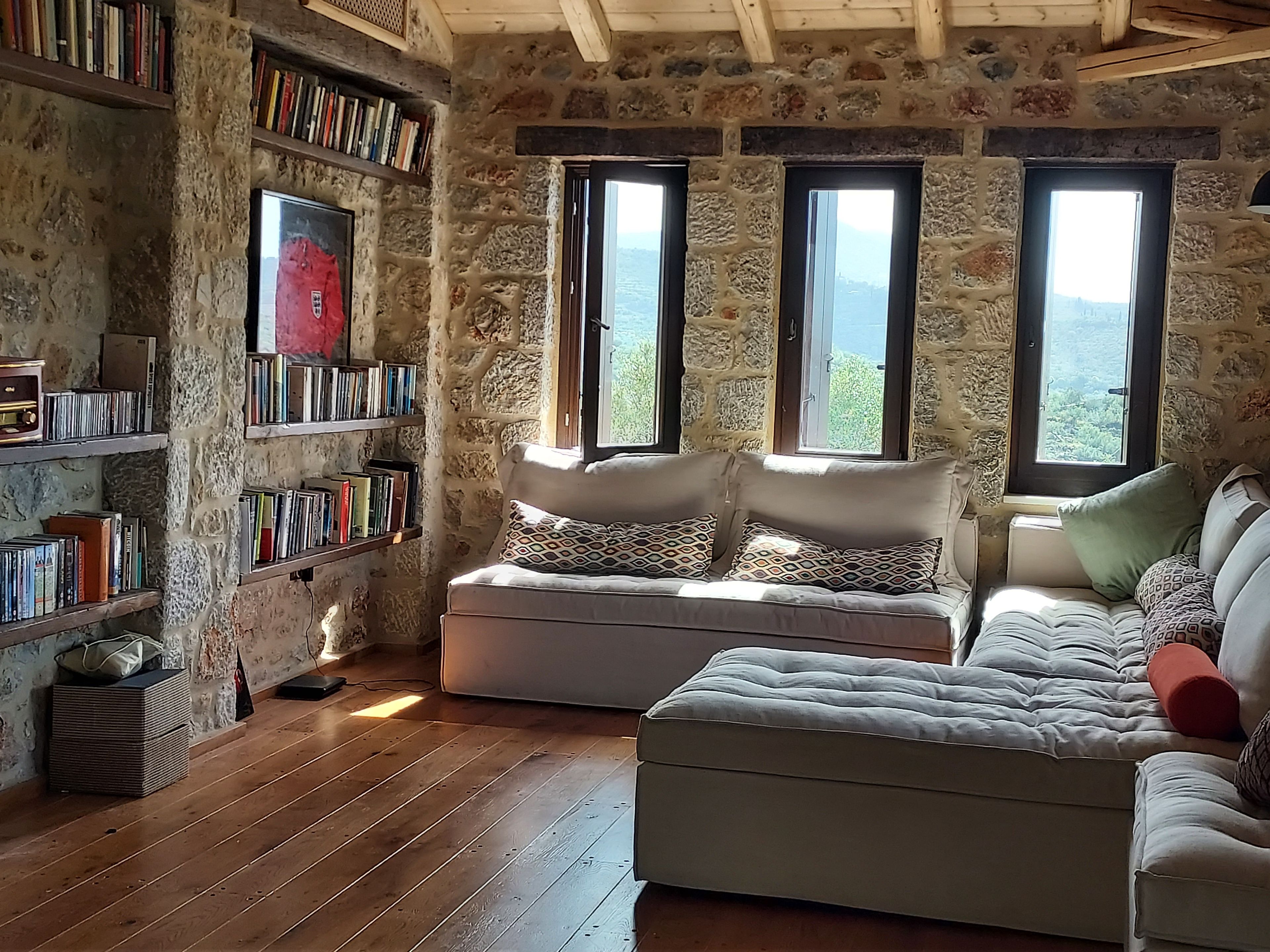 A cozy room with a stone wall, wooden floor, a sofa, and a bookshelf filled with books.