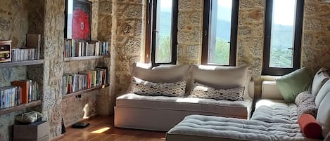A cozy room with a stone wall, wooden floor, a sofa, and a bookshelf filled with books.