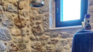 A stone-walled bathroom with a shower, a towel hanging on the wall, and a window with daylight. - Isolated luxury villa with pool, 30 mins to sea, 2 km to village shops tavernas (messenia)
