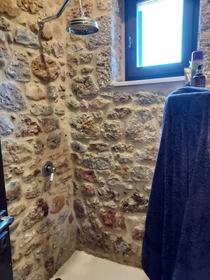 Een badkamer met stenen muren, een douche, een handdoek aan de muur en een raam met daglicht.