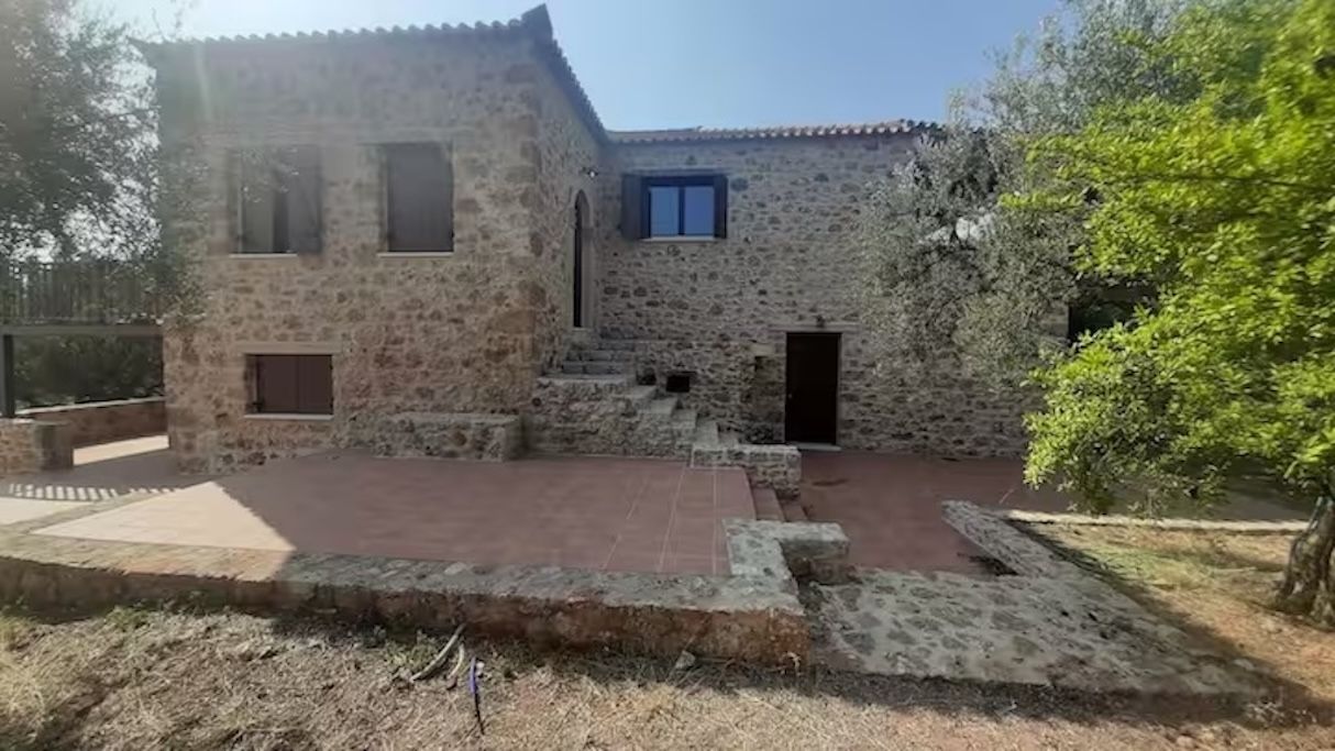 A stone building with a courtyard, a staircase leading to the entrance, and a small door.