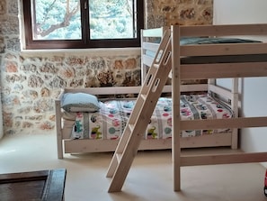 A bunk bed with a wooden ladder, a window with a view of trees, and a stone wall.
