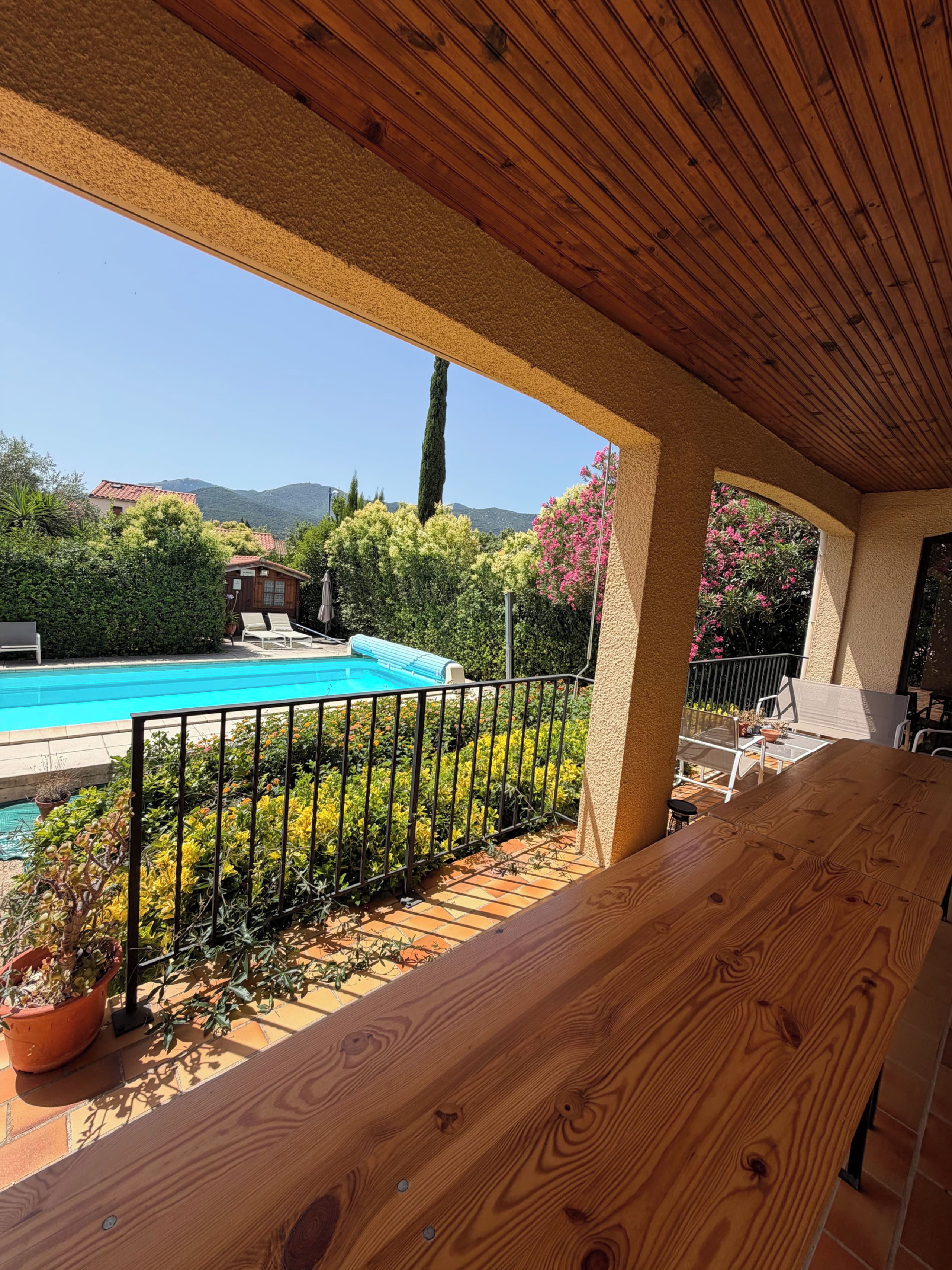 A wooden deck with a pool, surrounded by greenery and a view of mountains.
