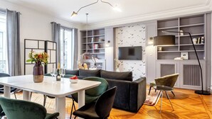 Ein modernes Wohnzimmer mit Essbereich, einer Couch, einem Fernseher und einem Bücherregal.