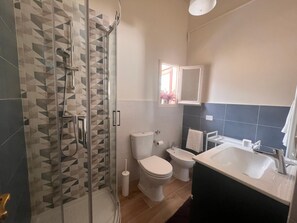 Ein Badezimmer mit Duschkabine, Toilette, Bidet und Waschbecken mit Spiegel.