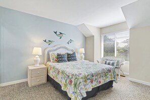 Ein Schlafzimmer mit einem Bett, Nachttischen, einem Sessel und einem Fenster mit Jalousien.