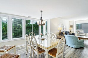 Un salón amplio con mesa de comedor, sillas y sofá. Hay una araña sobre la mesa y una lámpara en el sofá.