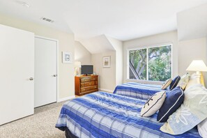 Un dormitorio con dos camas, un aparador, un televisor y una ventana con persianas.