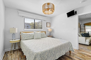 A bedroom with a bed, two bedside tables, a television, and a window with blinds. - Sunset Rentals | Hilton Head Resorts 3103 (Hilton Head Island)