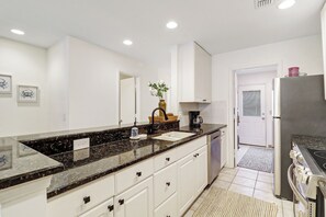 Eine moderne Küche mit weißen Schränken, einer Arbeitsplatte aus Granit und einem Edelstahlkühlschrank.