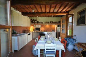 Cozinha com armários brancos, uma mesa de jantar posta para quatro pessoas e teto de madeira.