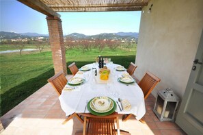 Uma área de refeições ao ar livre com uma mesa posta para seis pessoas, rodeada por cadeiras, com vista para uma paisagem deslumbrante.