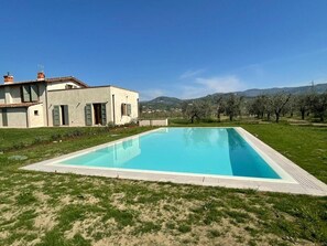 A rectangular swimming pool with a paved deck, surrounded by a grassy area with a building in the background. - Podere di Piero nel cuore delle colline lucchesi (LUCCA)