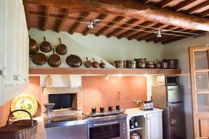 A kitchen with a brick wall, a stove, a refrigerator, and various pots and pans on the wall. - Podere di Piero nel cuore delle colline lucchesi (LUCCA)