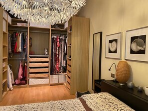 A bedroom with a bed, a bedside table, a lamp, and a wardrobe with hanging clothes. - Casa Romina nel cuore del centro storico (lucca)