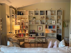 Uma sala de estar com sofá, poltronas, mesa de centro e estante repleta de livros e objetos decorativos.