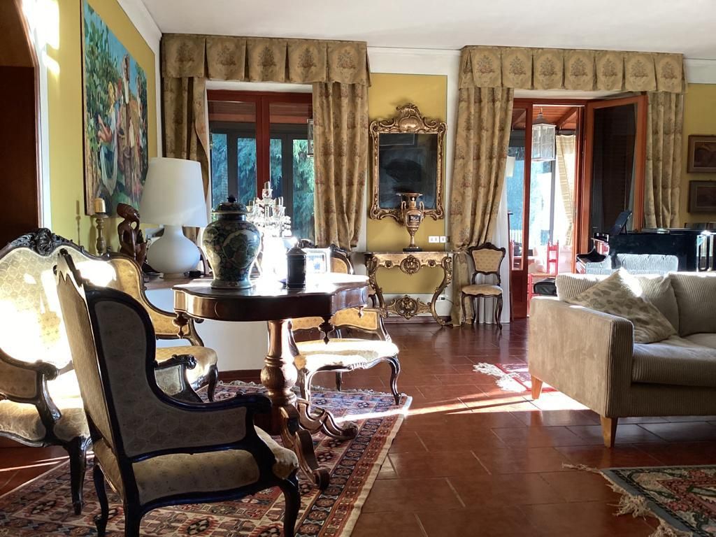 A traditional living room with a sofa, armchairs, a coffee table, and a dining table. There is a painting on the wall and a mirror above the table.