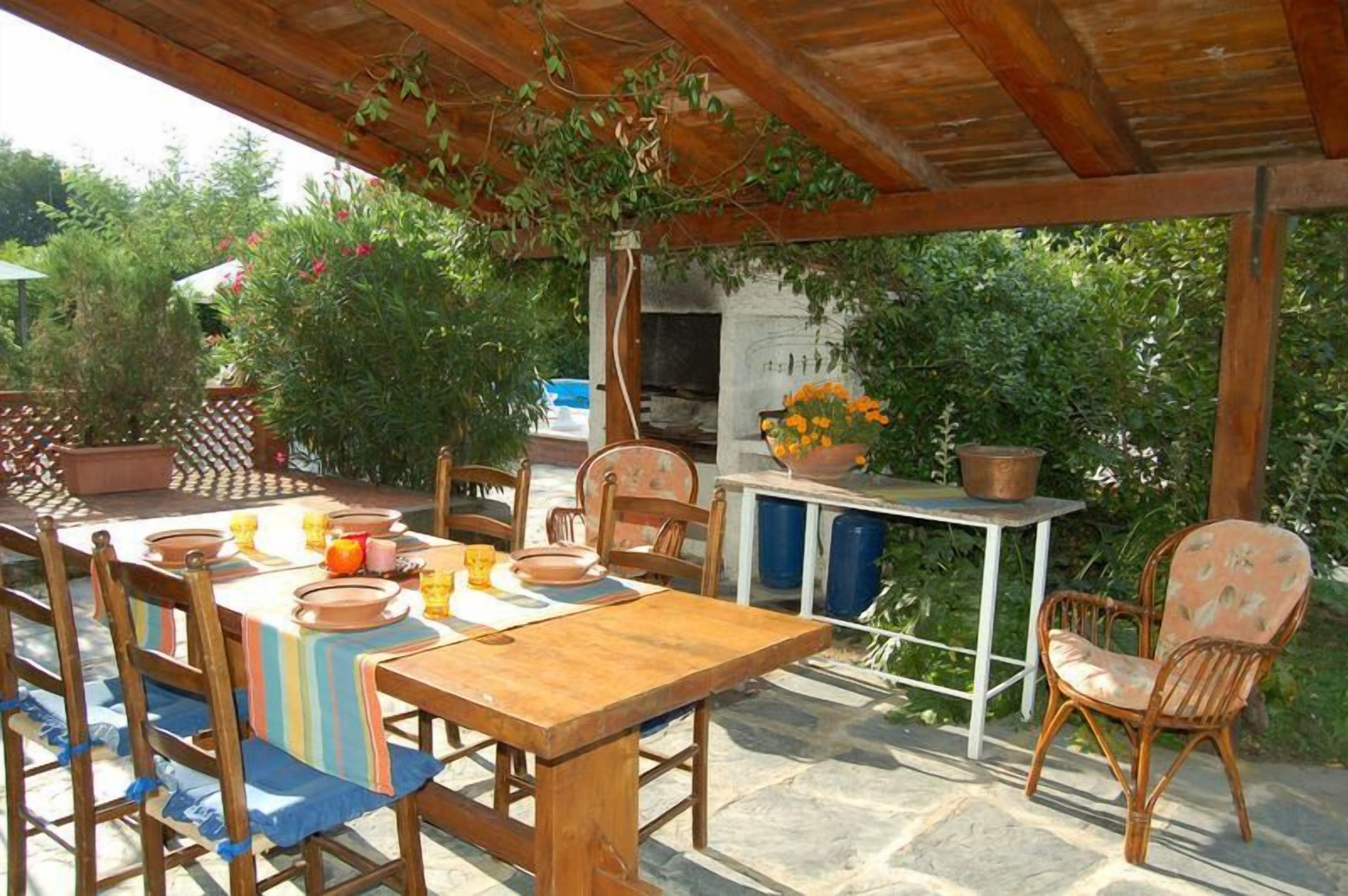 Eine Terrasse im Freien mit Holztisch und -stühlen, einem Grill und Kübelpflanzen.